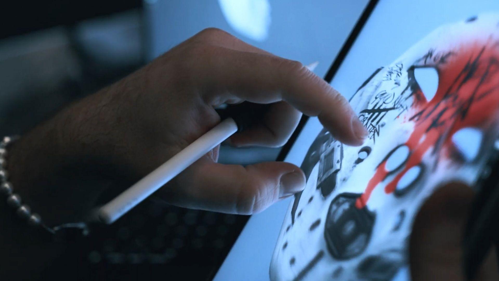 a hand holding a white pen with a digital drawing on a mask on a screen